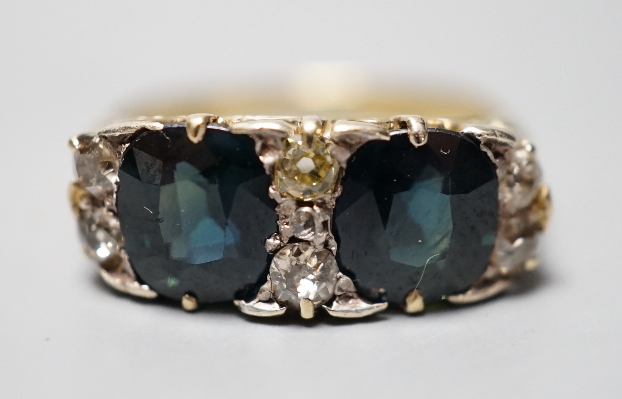 A yellow metal and two stone oval cut blue/green sapphire and seven stone diamond chip set half hoop dress ring, size Q, gross weight 5.7 grams